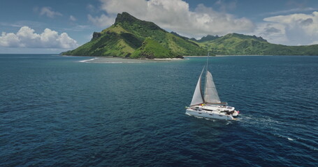Fiji: breathtaking aerial view catamaran sailing calm water near tropical island with green mountains, perfect representation of paradise. Remote wild nature exotic summer travel. Drone flight