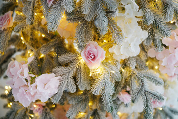 Pine branches with snow, soft pink and white flowers, and glowing warm lights