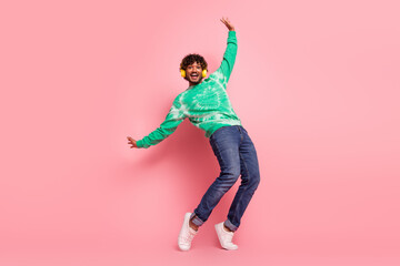 Happy young man dancing in a pink studio wearing a green tie dye sweater jeans and white sneakers...