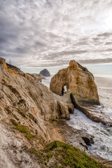 A rocky cliff overlooks the ocean with a cloudy sky in the background. The scene is serene and peaceful, with the waves crashing against the rocks and the wind blowing through the grass