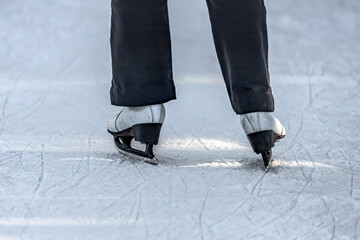 Ice skating shoes. Legs in skates. Winter outdoor activities. Winter vacation. Ice skating in winter. Sports equipment. Figure skating. Rear view of legs in skates riding on an ice rink.