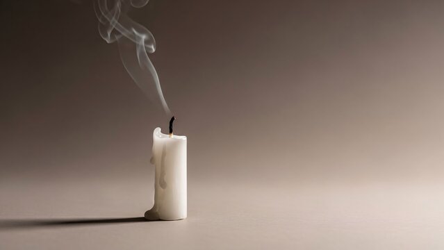 Extinguished white candle with smoke on a gray background symbolizing loss or farewell