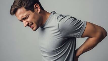 Man clutches his lower back, grimacing in pain, on a gray backdrop
