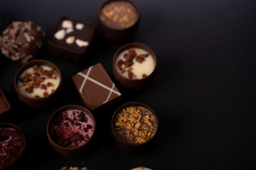 close-up of assorted gourmet chocolate pralines and truffles on a matte-black studio backdrop,...