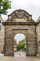 Obraz premium A stone archway in Hanover Germany with a crown on top of it. The archway is in front of a building with a red roof