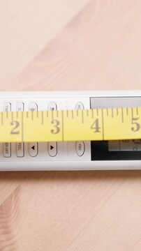 Person with measuring tape measure size of remote controller on table