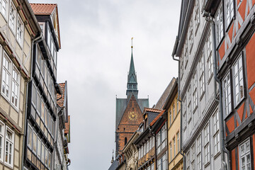 Obraz premium A street in Hanover with a tall clock tower in the background. The street is lined with old buildings, some of which have green lanterns on top. The scene has a nostalgic and historic feel to it