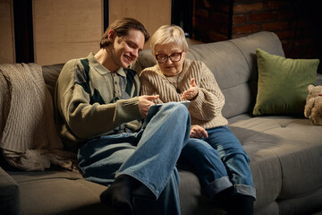Grandmother explaining tablet content to grandson at home. Concept of reverse learning, intergenerational exchange, shared technology use, warm family interaction indoors.