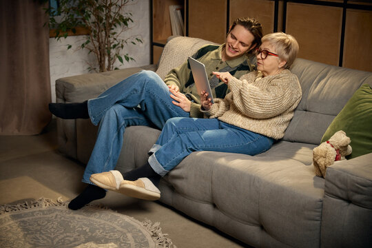 Grandmother pointing at tablet while sitting with grandson. Concept of intergenerational communication, shared digital experience, family learning, everyday home life.