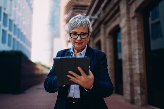 Senior female executive using digital tablet on city street, demonstrating modern business adaptability, remote work flexibility, and confidence in digital collaboration. - Powered by Adobe