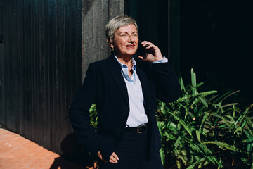 Smiling senior woman speaking on smartphone outdoors, symbolizing professional connection, remote engagement, and confidence in digital communication in real-time settings.