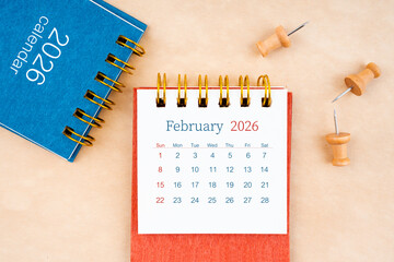 February 2026 desk calendar with wooden thumbtack on brown paper.