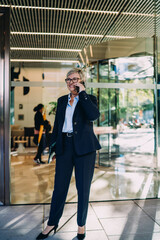 Full-body shot of senior woman smiling during phone call, holding tablet, exemplifying digital multitasking, mobile readiness, and humanized tech use in modern business.