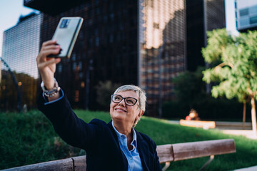 Smiling senior woman taking selfie outdoors, representing tech engagement, professional identity, and digital presence in today’s connected and mobile business world.
