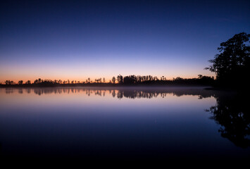 A beautiful lake with a dark sky in the background. The sky is filled with clouds and the sun is setting