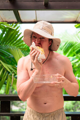 Scandinavian Tourist Man Eating Durian Outdoors with Tropical Leaves Background