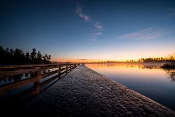 A beautiful sunset over a lake with a wooden pier. The water is calm and the sky is filled with clouds