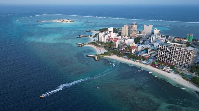 Maafushi, Maldives: Aerial drone footage of hotels in Maafushi, a local island in Kaafu Atoll of maldives. With backward and tilt up motion showing white sand beach and a boat leaving the island