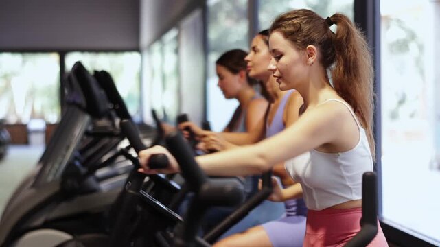Determined young girls training with air bike in fitness hall during workout session. High quality 4k footage
