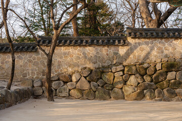 Ancient stone wall with traditional tile roof and bare trees creates a tranquil courtyard scene during daytime.