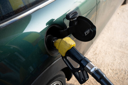 Close-up of a green compact car being refueled at a gas station. Fuel nozzle inserting into the car's fuel tank.