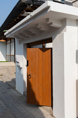 Warm wood door contrasts crisp white walls, creating an inviting entrance to a home on a sunny day.