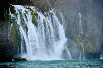 Powerful cascading waterfalls crashing over moss-covered rocks into a turquoise pool below. Kravica Waterfalls, Bosnia and Herzegovina