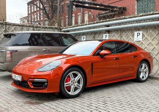  Hybrid Porsche Panamera 4S orange color parked at the city street. Orange car Porsche Panamera 4S on parking lot. The modern exterior of a premium German premium car. 