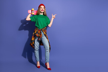 Young woman with skateboard cheerfully in casual streetwear purple backdrop wear shirt jeans red...