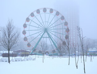 A snow-covered deserted park with a Ferris wheel on a foggy winter day, Yesenin Park, Saint Petersburg, Russia, January 19, 2026