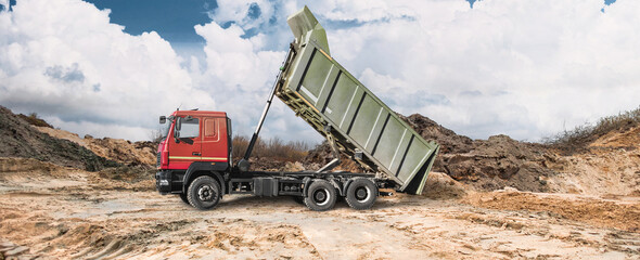 At the construction site, a dump truck can be seen dumping earth onto the site, creating earthen embankments, while the sky is overcast. Heavy equipment is working on the site © Anoo