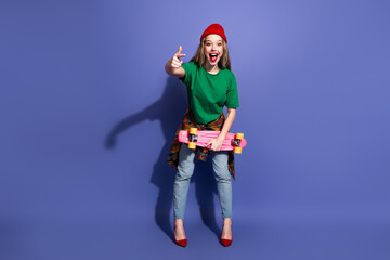 Young girl with skateboard purple background wear green shirt red beanie plaid shirt tied at the...