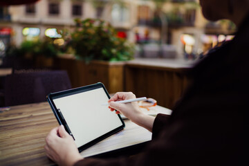 Detailed close-up of woman using stylus on tablet at cafe table, focusing on digital interface, precise motion, and personal control in mobile creative work.