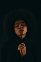 Young woman with stunning afro hairstyle showcases bold fashion in a striking dark setting