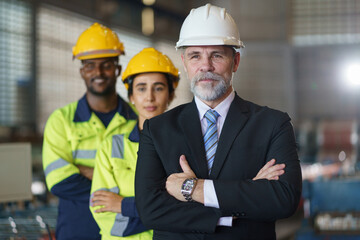 A foreman and worker are standing in a factory, looking standing pose. They wear a yellow and white safety helmet for safety.