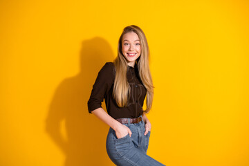 Young smiling woman in casual shirt and jeans stands against a bright yellow background for fashion...