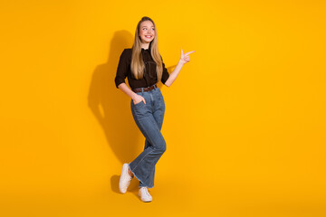 Young woman in casual fashion points to the right against a bright yellow background