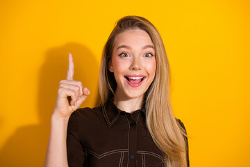 Young smiling woman points up with her finger against a bright yellow background ready to share...