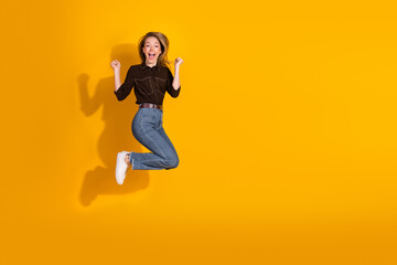 Jumping young woman in casual outfit celebrates excitement against bright yellow background