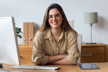 Beautiful business woman working with computer while looking at camera at the office