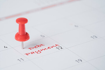 Debt payment reminder marked on calendar with red push pin representing financial obligation, loan...