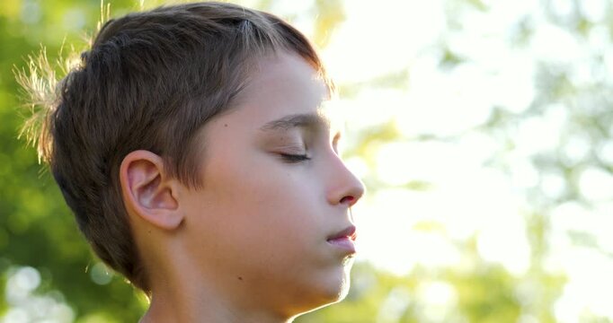 Child portrait in summer park at sunset. Child boy portrait shows calm profile and soft bokeh. Warm golden light touches skin hair. Family marketing education. Thoughtful silhouette kid outdoors.