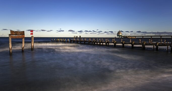Wooden sign in the sea with inscription Zingst and wooden walkway, pier with diving gondola behind, panorama, long exposure, evening light, Zingst, Fischland-Dar&szlig;-Zingst, Western Pomerania Lagoon Area National Park, Mecklenburg-Western Pomerania, Germany