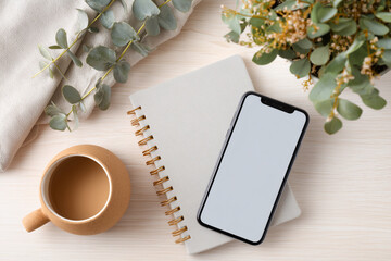 A phone and a notebook are on a table with a plant in the background