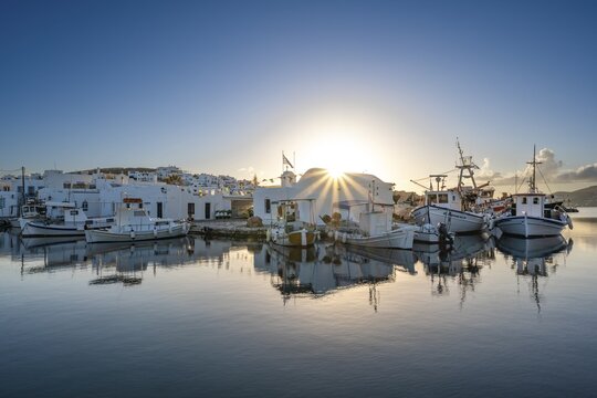 Fishing boats in the harbour of Naoussa at sunset, reflected in the sea, Sun star, White Cycladic houses, Naoussa, Paros, Cyclades, Greece