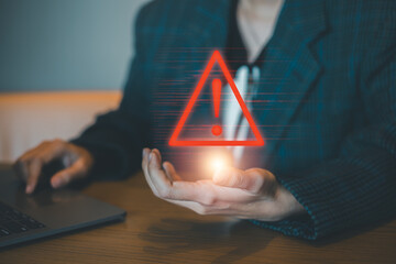 A businessman holds a glowing digital warning sign, symbolizing alert and caution in a modern office environment.
