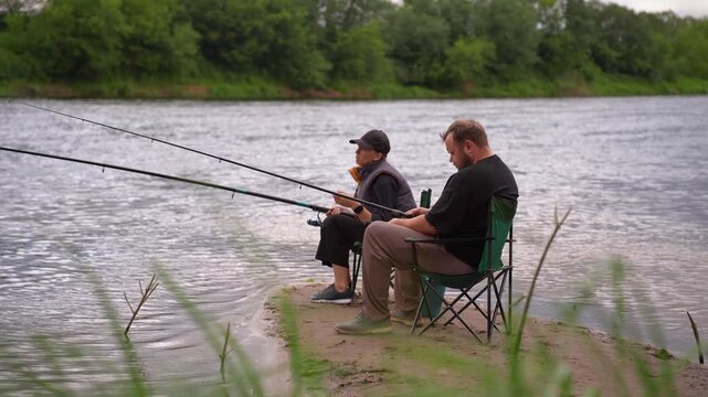 Man and woman spending quality time together, fishing with rods from the sandy bank of a river on a cloudy day, enjoying their outdoor hobby, leisure, and a quiet weekend retreat