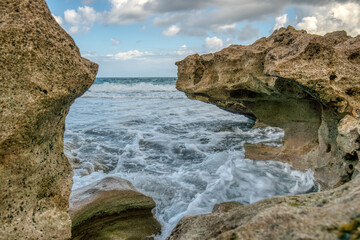 Fototapeta premium The ocean is rough and the rocks are jagged. The waves are crashing against the rocks, creating a powerful and dynamic scene. The water is a deep blue color, and the sky is a clear blue color