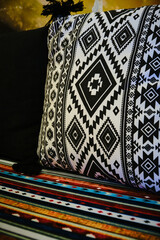 Close-up view of decorative cushion featuring bold black-and-white geometric tribal patterns placed against multicolored textile. Ethnic interior styling with rich textures and vibrant color contrasts