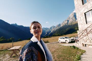 Woman portrait in the mountains beside a stone cottage and parked car, wearing a patterned jacket...